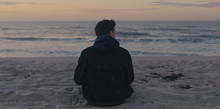 Man sitting at the beach with his back to the camera.